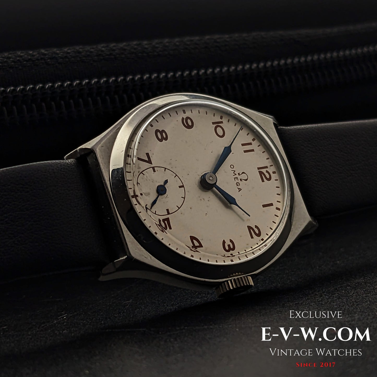 Vintage Omega wristwatch resting on a black leather surface, showcasing its classic Art Deco design with a silver dial and blue hands.