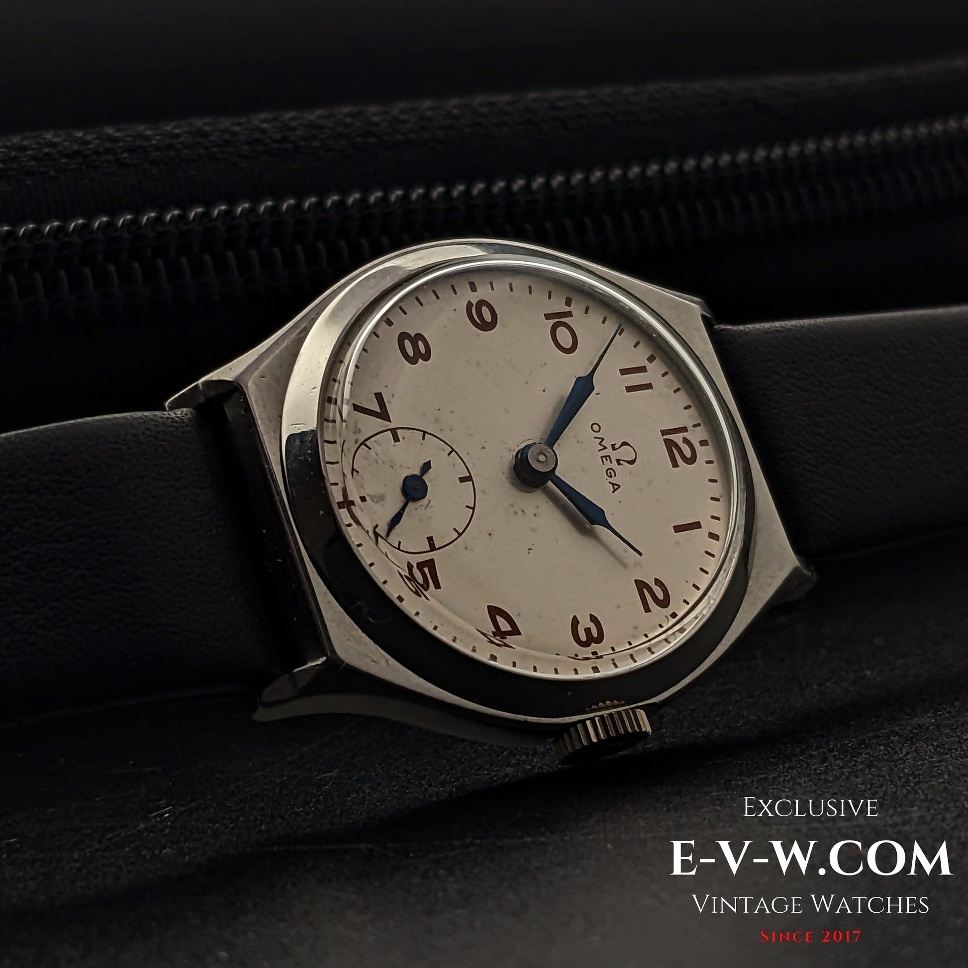 Vintage Omega wristwatch resting on a black leather surface, showcasing its classic Art Deco design with a silver dial and blue hands.