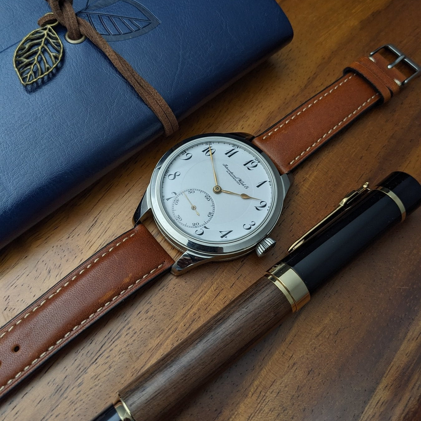 Watch with brown leather strap and blue notebook on wooden surface